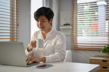 Handsome Asian businessman sipping coffee and working on his business tasks on laptop