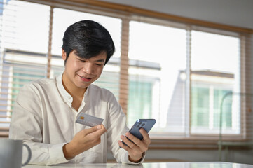 Happy Asian man using mobile banking application to transfer money or pay online bills.