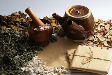 Decoction pot, mortar and pestle surrounded by dried herbs, medicine package on light background....