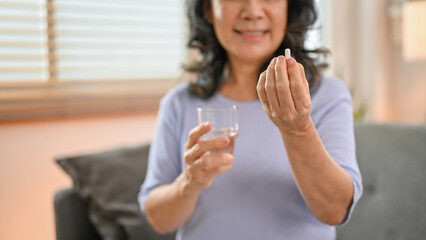 Close-up image, a happy 60-year-old retired Asian woman holding a glass of water and a pill