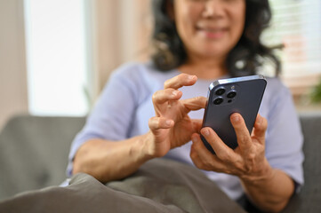 Cropped image of a happy 60-year-old retired Asian woman using her phone on a sofa