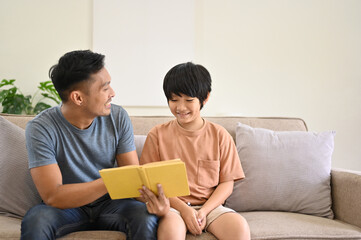 Fototapeta premium Happy Asian dad is talking and telling a story to his son on a sofa in the living room.