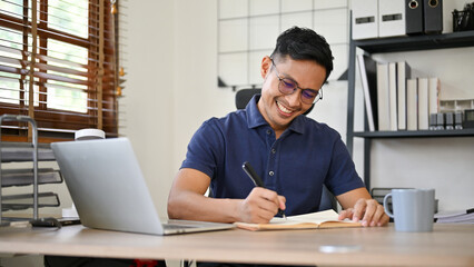 Smart Asian businessman writing something on notebook, working on his business tasks