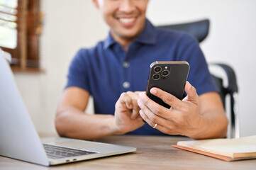 Close-up image of a smiling millennial Asian businessman using his phone at his workspace