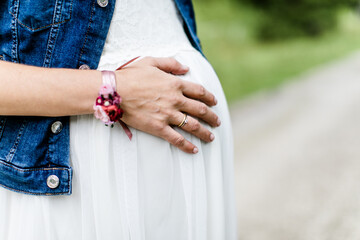 Hand auf dem Babybauch einer schwangeren Braut im weißen Kleid Jeansjacke