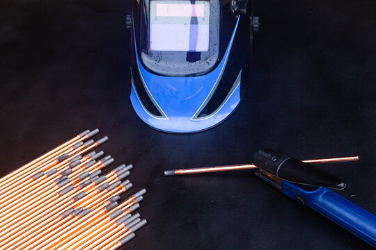 Graphite gouging electrodes with holder and welding mask on black background.