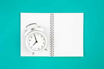 Fototapeta na wymiar Notebook and alarm clock on a blue background, flat lay.