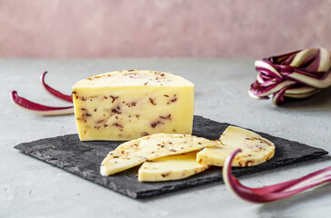 Italian traditional soft cheese Caciotta with radicchio cut on stone board, grey and rose background and fresh radish