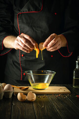 The cook pours a raw egg into a bowl. Delicious breakfast menu idea for hotel or restaurant on black background