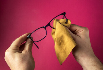 Close-up of a person's hands wiping dust off glasses with a napkin. Reading glasses on red...