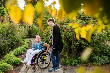 Disabled woman in wheelchair with assistant in garden