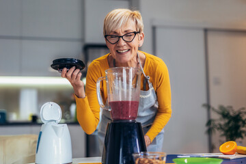 Senior woman in casual home clothes prepares healthy cocktails with different seasonal fruits.