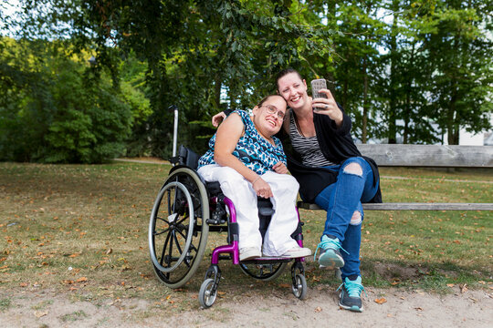 Disabled woman in wheelchair with assistant photographing self in park