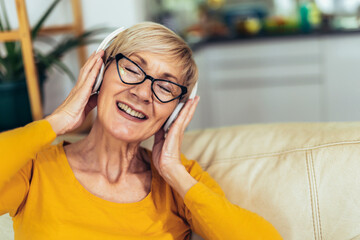 Happy elderly female in headphones smiling listening to music at home
