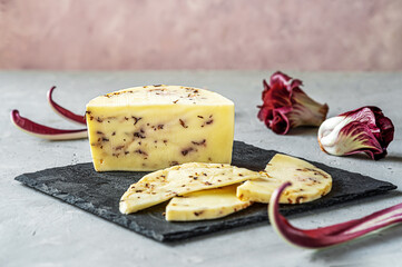 Italian traditional soft cheese Caciotta with radicchio cut on black stone board, grey and rose background and fresh radish