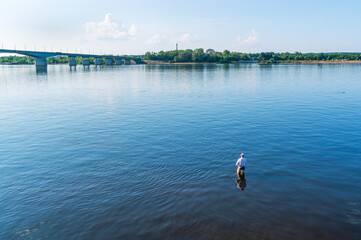 A fisherman is fishing with a fishing rod in shallow water. Fishing on the river. In summer, relax on the river bank. A man goes fishing on the weekend.