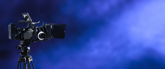 Digital movie camera filming in the dark with smoke and blue lightning background. television, broadcast, video, film studio or movie production background with copy space