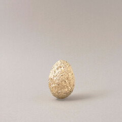 Golden egg with interesting texture on a gray background. Creative food concept.