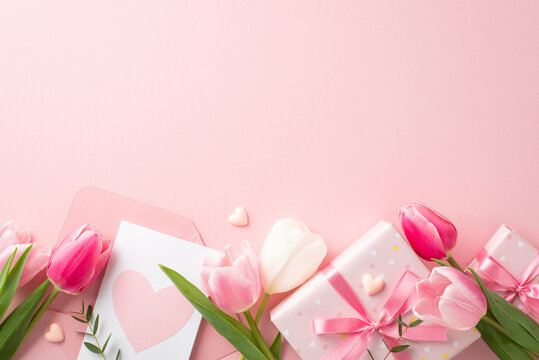 Mother's Day celebration concept. Top view photo of gift boxes with bows envelope with postcard fresh flowers tulips and small hearts on isolated pastel pink background with blank space