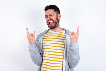 Naklejka premium Young caucasian mán wearing trendy clothes over white background making rock hand gesture and showing tongue