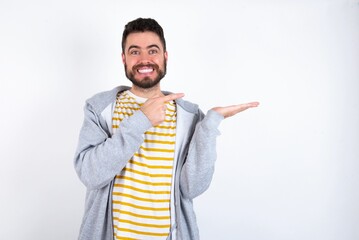 Young caucasian mán wearing trendy clothes over white background pointing and holding hand showing adverts