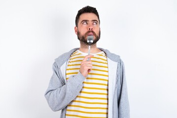 Very hungry Young caucasian mán wearing trendy clothes over white background holding spoon into mouth dream of tasty meal