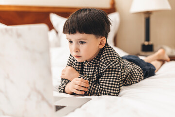 Smart looking preschool boy lying on the bed using notebook computer in his room looking at the screen. Online learning, Home preschool, New normal, Home Based Learning