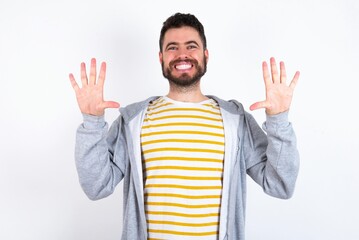 Naklejka premium Young caucasian mán wearing trendy clothes over white background showing and pointing up with fingers number ten while smiling confident and happy.