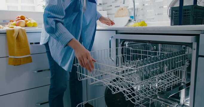 Woman uploading dishwasher dirty plates, housewife uses modern appliance for timesaving