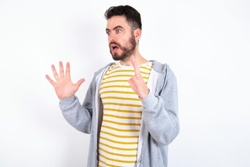 Young caucasian mán wearing trendy clothes over white background shouts loud, keeps eyes opened and hands tense.