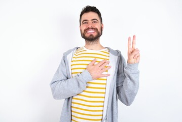 Young caucasian m&aacute;n wearing trendy clothes over white background smiling swearing with hand on chest and fingers up, making a loyalty promise oath.