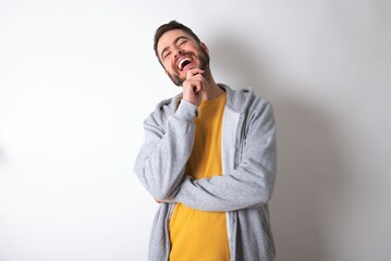 Young caucasian m&aacute;n wearing trendy clothes over white background laughs happily keeps hand on chin expresses positive emotions smiles broadly has carefree expression