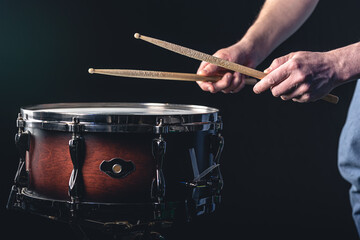 A man plays the snare drum against a dark background.