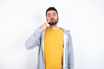 Charming Young caucasian mán wearing trendy clothes over white background pointing on pout lips with forefinger, showing effect after lifting procedure,