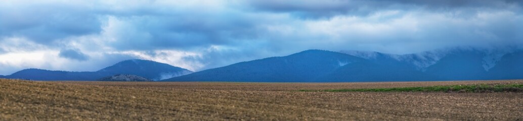 Panoramic view of mountains with storm clouds and crop fields in foreground in autumn