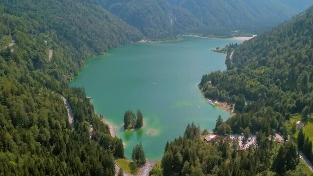 Aerial 4K footage of Lagodel Predil in Italy showcases the stunning alpine lake, nestled among the snow-capped peaks of the Julian Alps, surrounded by the natural beauty of the region.