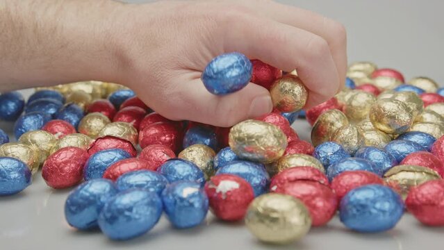 Hand grabbing a lot of chocolate easter eggs from a pile of shiny wrapped and colorful eggs