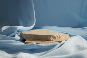 Broken stone podium decorated on light blue fabric texture luxurious background. Blank stage, platform or pedestal for display product.