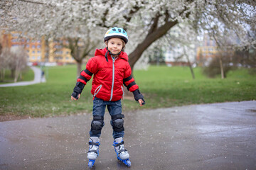 Little child, preschool boy in protective equipment and rollers blades, riding on walkway