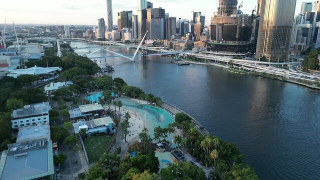 Drone shot of Brisbane City's South Bank Beach and Parklands. Camera orbiting the artificial beach. Brisbane City River in background. Queens Wharf Casino and Neville Bonner Bridge in development.