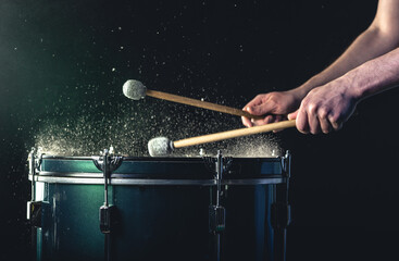 A man plays a musical percussion instrument with sticks on a dark background.