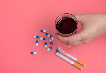 Kieliszek wina trzymany w dłoni na różowym tle obok papierosów i tabletek 