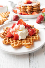 Strawberry dessert with fresh baked waffles, whipped cream and strawberry sauce on a plate on white table background