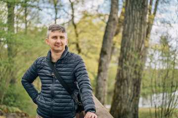 A middle-aged man with a gray hair in a thin down jacket in early spring surrounded by trees