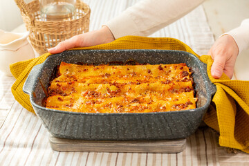Woman hands with just baked hot lasagna in a casserole. Homemade lasagne made with meat bolognese...