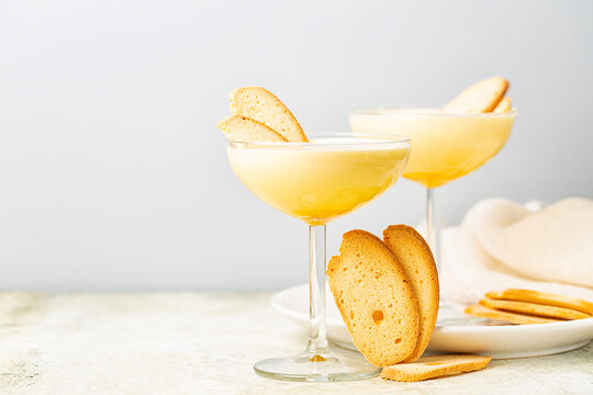 Zabaione or sabayon, or advocaat in a champagne coupe, alcoholic creamy drink  or dessert. Cream made with egg yolks, sugar, and a sweet wine Marsala or liqueur. Baicoli biscuits. White backhground.
