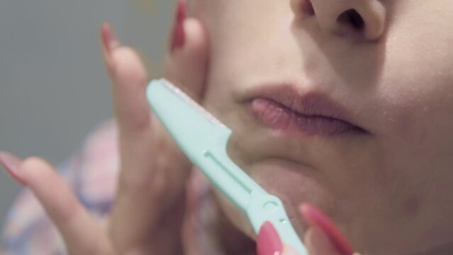 The 4k footage of a woman using a facial razor to shave the hair on her face during her skincare routine