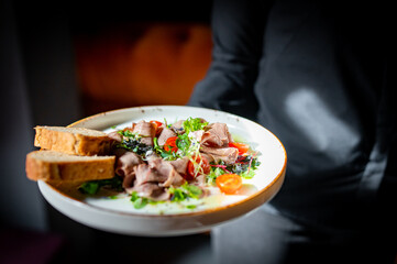 Waiter holds a plate with salad in the restaurant.