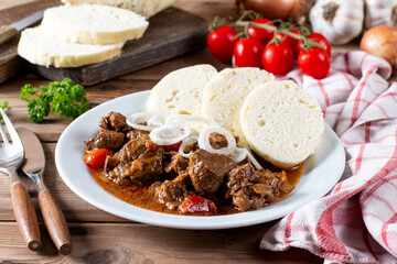 Czech traditional goulash with breaded dumpling and onion on white plate on table