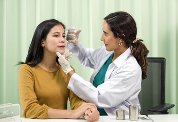 Doctor in white gown and protective glove giving female patient medical injection in forehead.